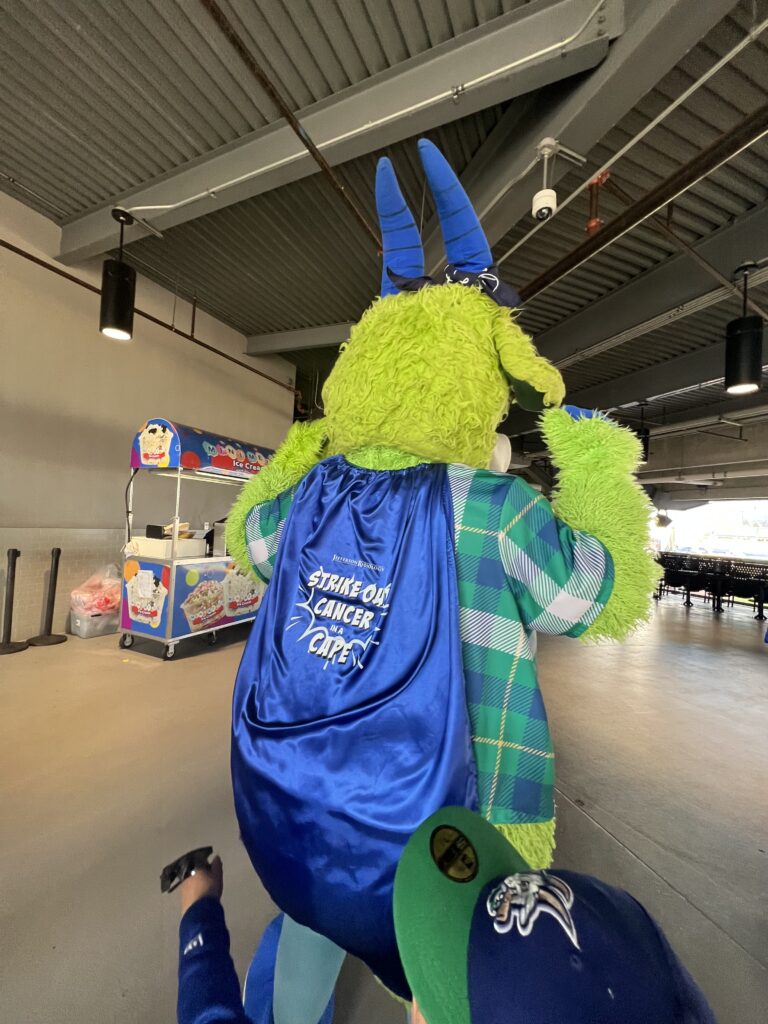 Chompers, the YardGoat mascot wearing a strike out cancer cape.